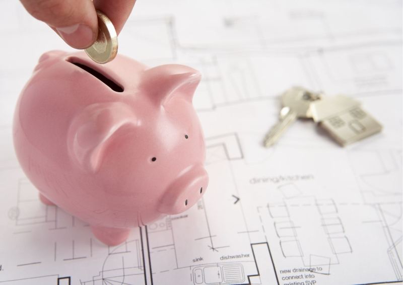 Pink pig on set of home plans with person putting a coin in it.