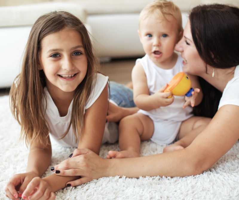 Mother & 2 kids laughing while lying on carpet
